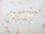 close up of a creamy white bar of soap with oatmeal flakes in it