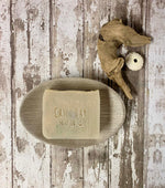 Bar of soap with 'Cascadia Soap Co' branding on a wooden soap dish against a rustic wooden background.