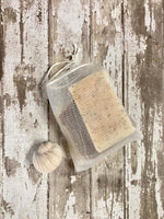 White mesh pouch with a drawstring opening filled with soap ends and slivers shown displayed on a distressed wooden surface