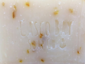 close up of a creamy white bar of soap with yellow flower petals