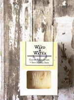 a white box with a cutout shows a creamy white bar of soap with yellow flower petals
