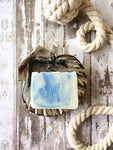 a creamy white bar of soap with blue swirls sits in a silver shell shaped soap dish