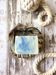 creamy white soap bar with blue swirls sits in a soap dish