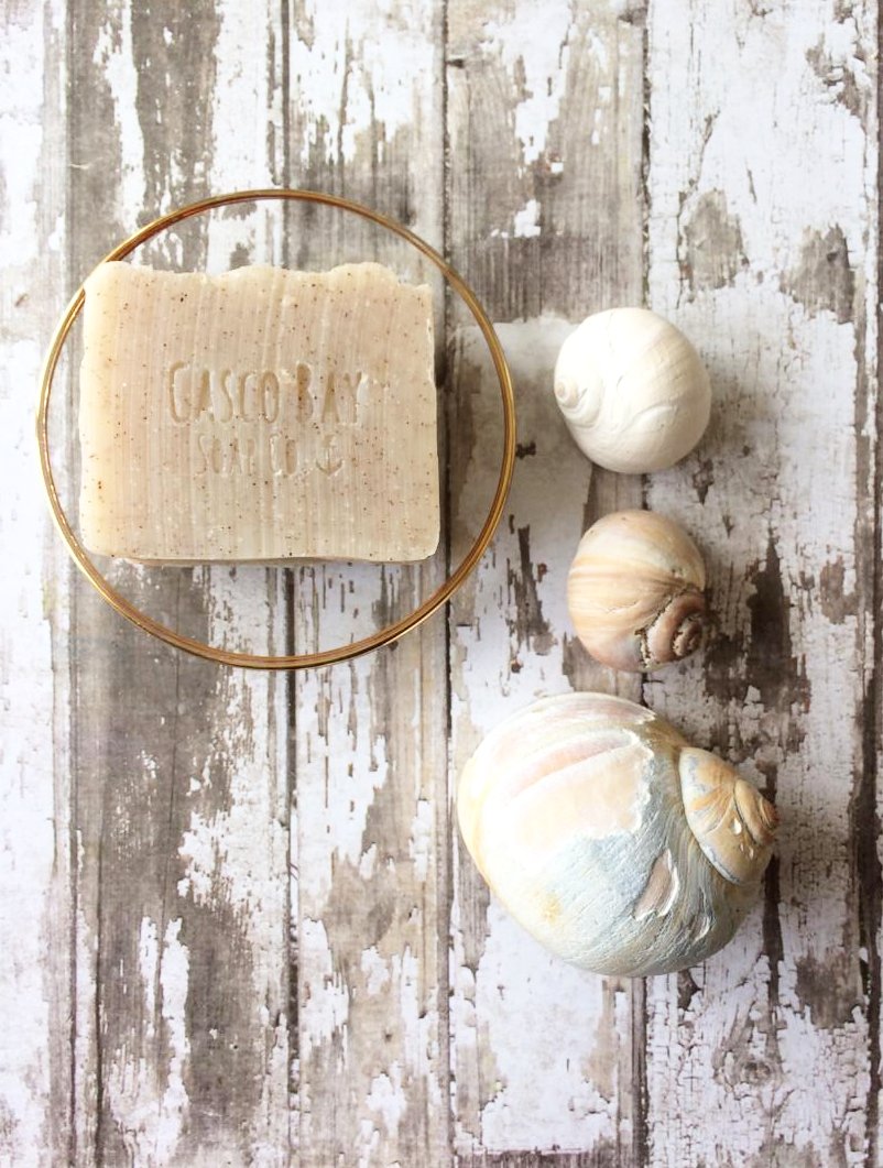 a light tan bar of soap with brown flecks sits in a round glass soap dish