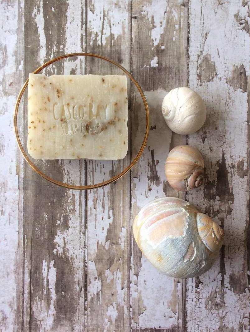 a off white bar of soap with flecks of green sits in a glass soap dish