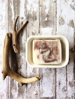 a creamy white bar of soap with brown swirls sits in a soap dish