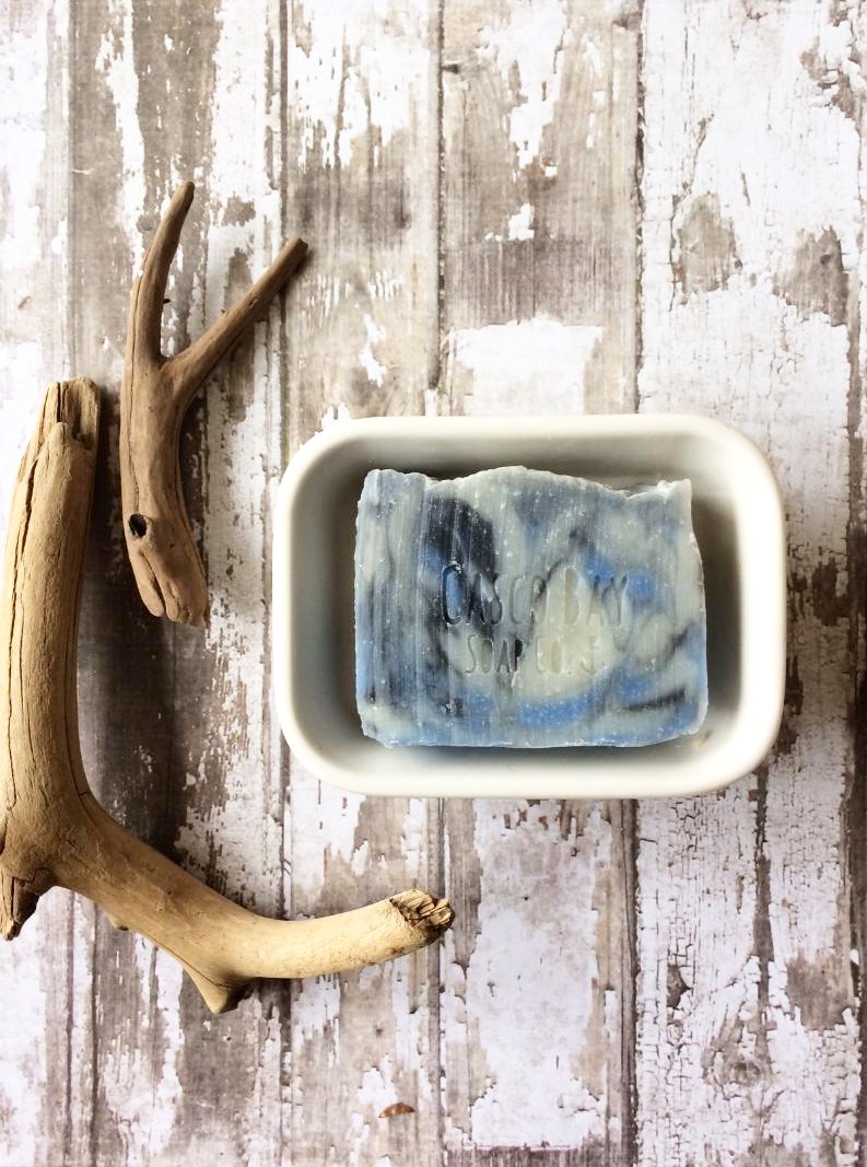 creamy white bar of soap with blue and black swirls sits in a white soap dish