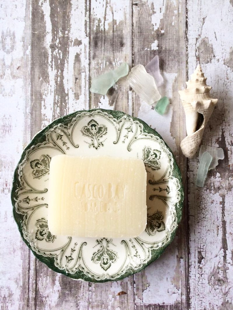 a creamy white bar of soap sits in a vintage green and white soap dish