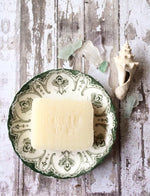 creamy white bar of soap sits in a vintage green and white dish