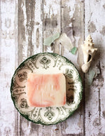 an off white bar of soap with red swirls sits in a vintage green and white soap dish