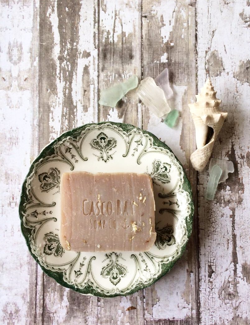 a tan bar of soap with oatmeal flakes in it sits in a vintage green and white dish