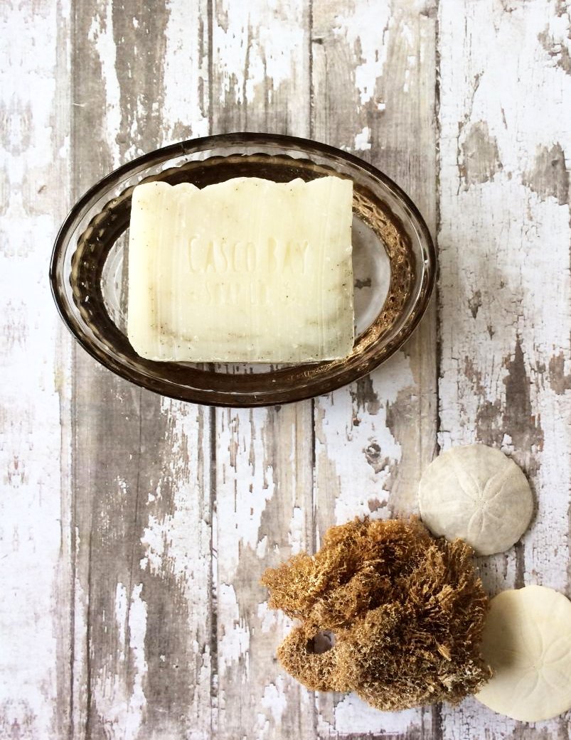 a creamy white bar of soap with mossy green swirls and flecks sits in a soap dish