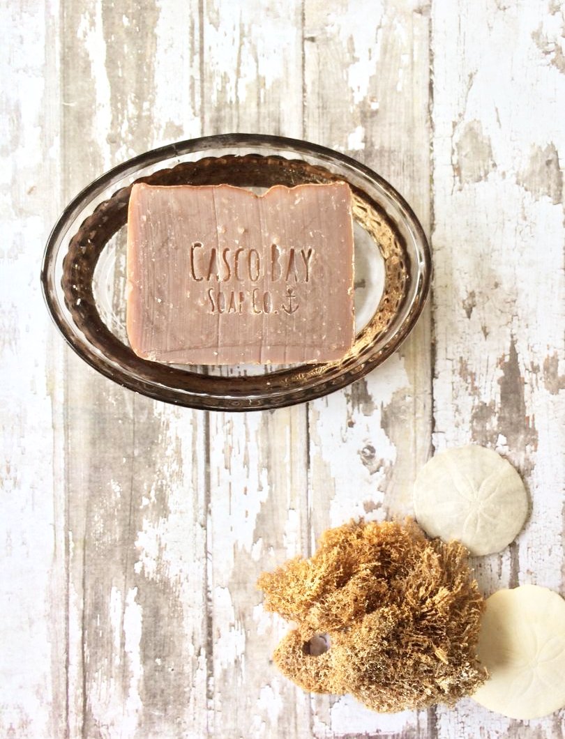 a tan bar of soap sits in a glass oval soap dish