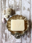 a creamy white bar of soap sits in a silver soap dish