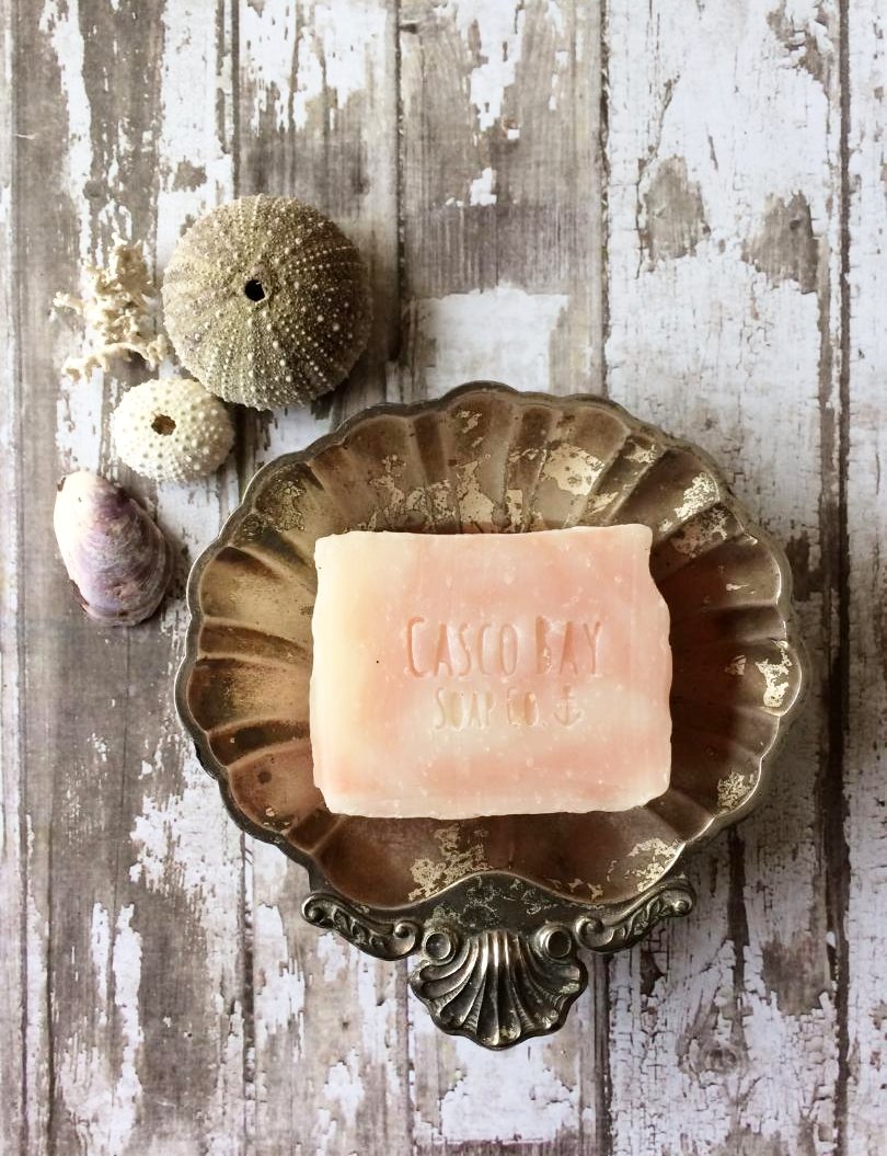 a creamy white bar of soap with pink swirls sits in a silver shell shaped soap dish