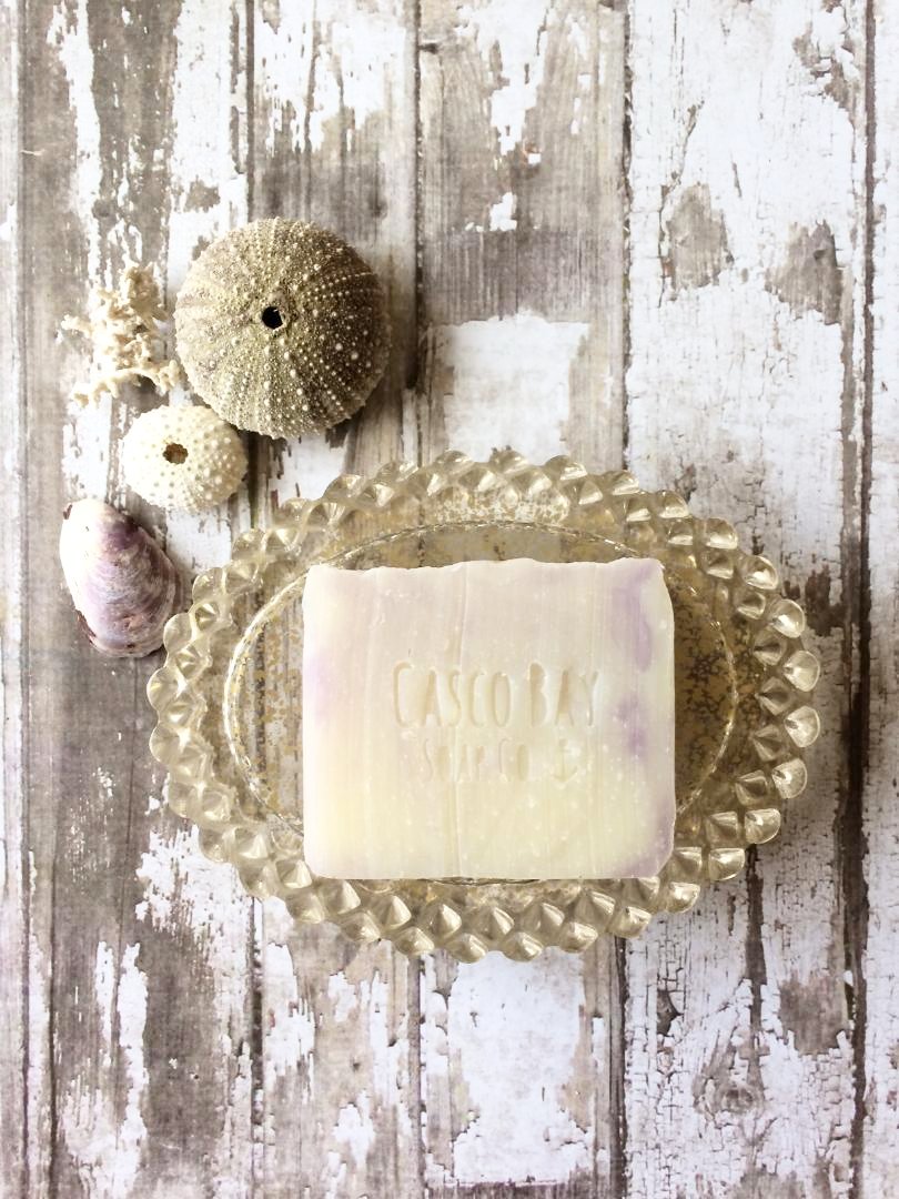 a creamy white bar of soap with purple swirls sits in a gold soap dish