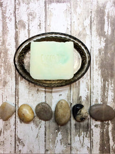 a creamy white bar of soap with bright green swirls sits in an oval soap dish