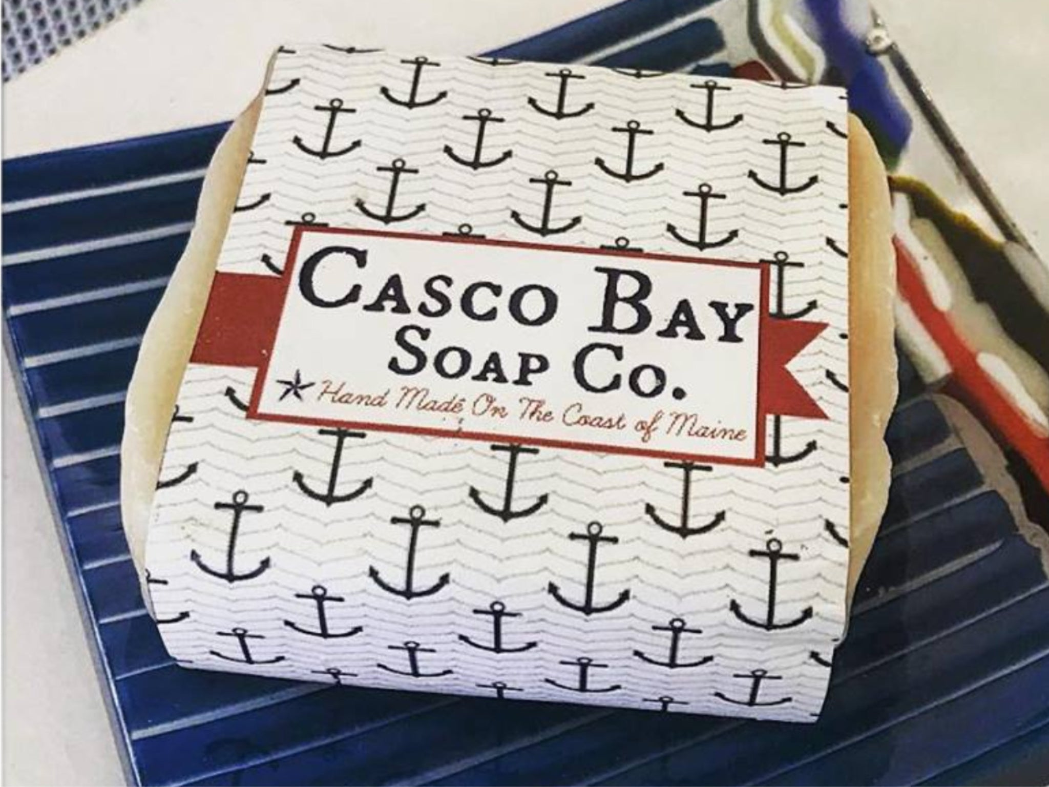 close up of bar of soap with white paper label with blue anchors and company logo on it