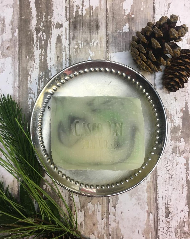 off white bar of soap with black and green swirls sitting in a silver soap dish
