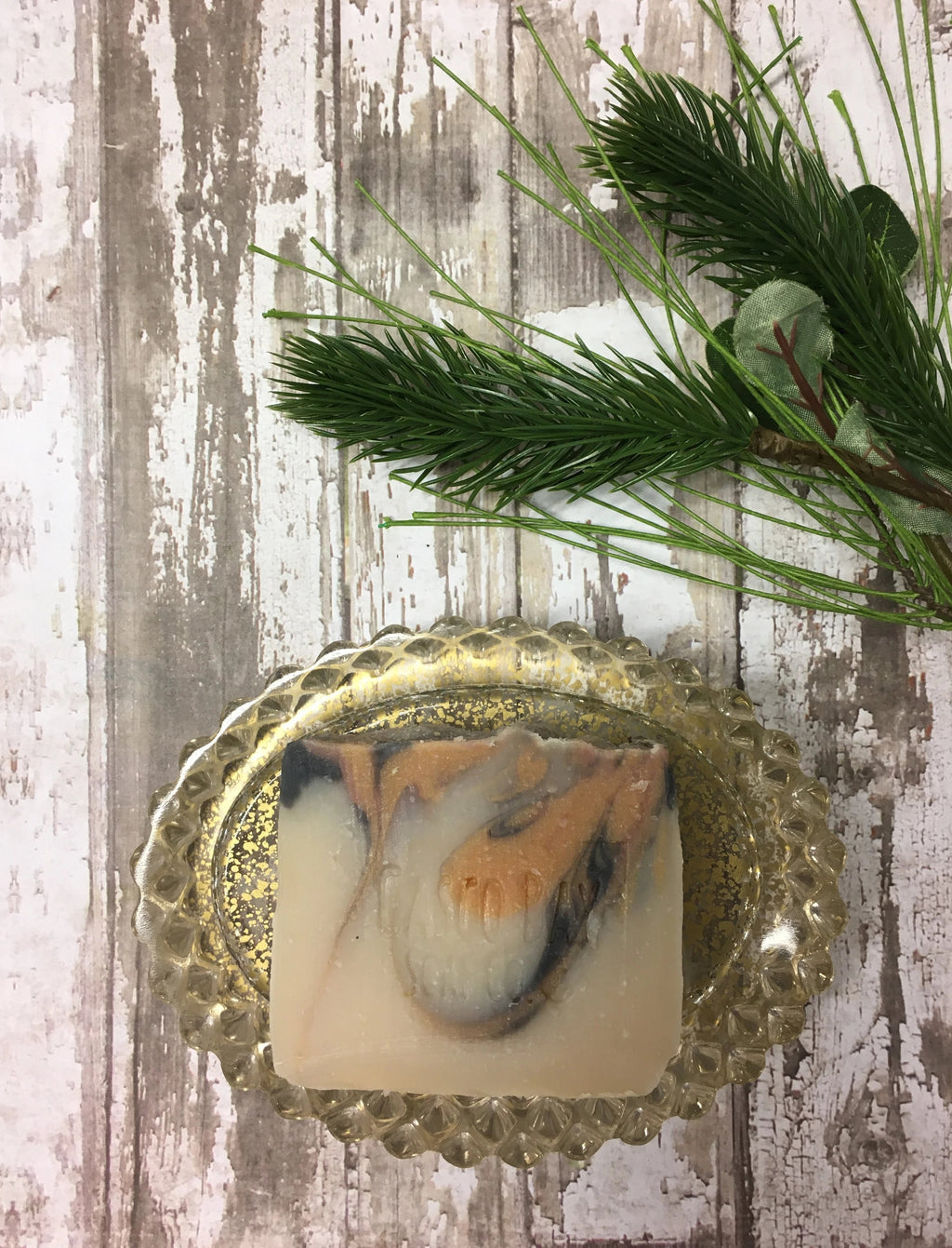a creamy white bar of soap with black and orange swirls sits in a gold flecked soap dish