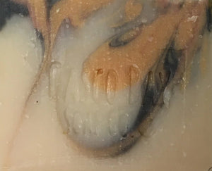 close up of a creamy white bar of soap with orange and black swirls