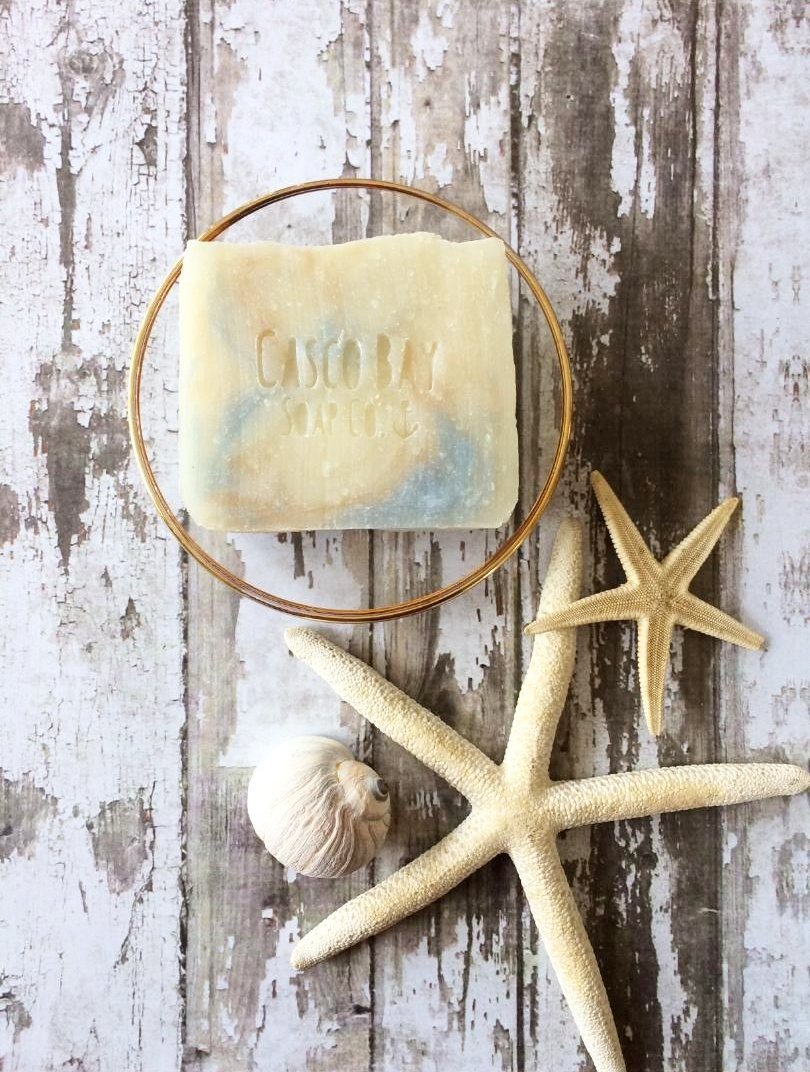 a creamy white bar of soap with brown and blue swirls sits in a round glass soap dish