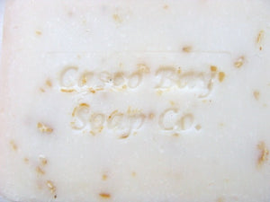 close up of a creamy white bar of soap with oatmeal flakes in it