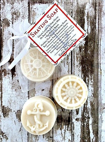 3 creamy white round bars of soap each adorn with a different image an anchor a ships wheel and a compass one soap is shown inside a white orangza bag 